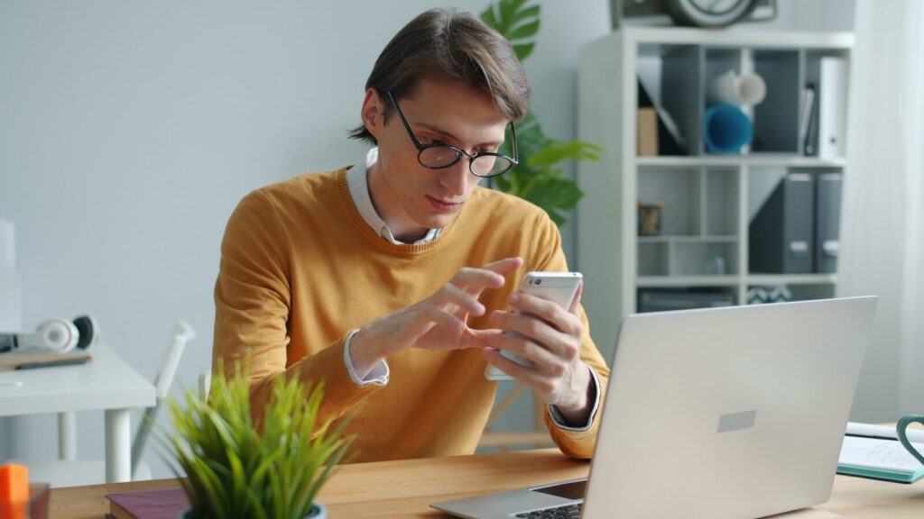 Man in yellow sweater using smartphone at desk